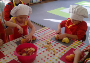 Dzieci przy stole podczas krojenia owoców .